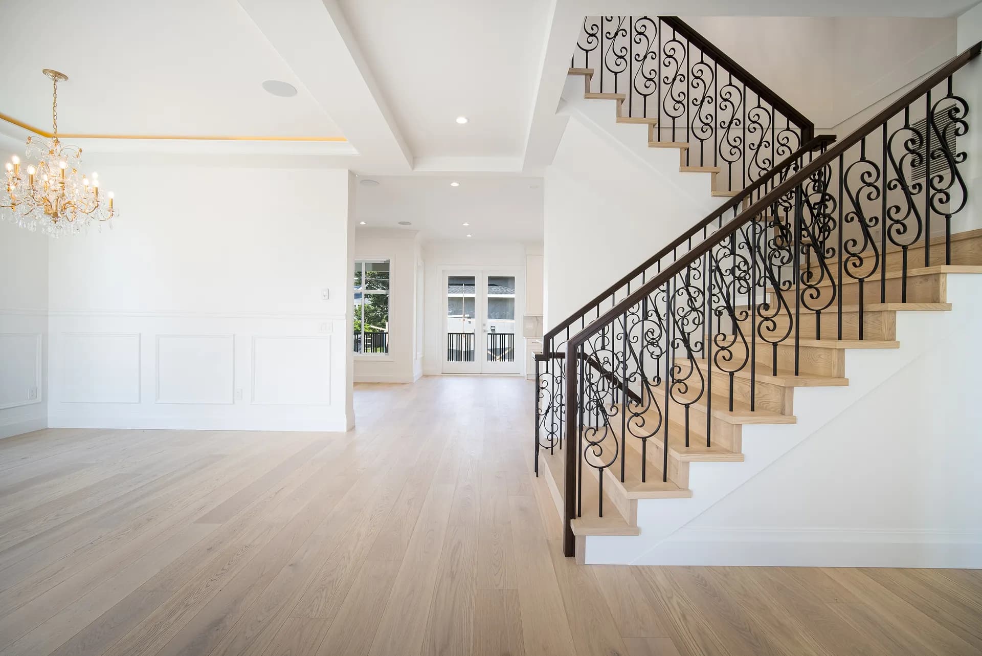 Oak staircase with ornate wrought iron balusters and foyer chandelier