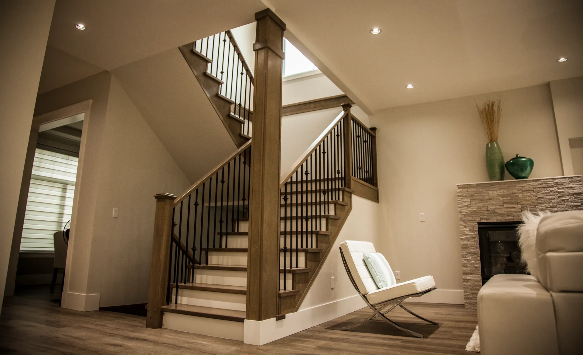 Open staircase with stained wood posts and iron spindles beside the stone fireplace
