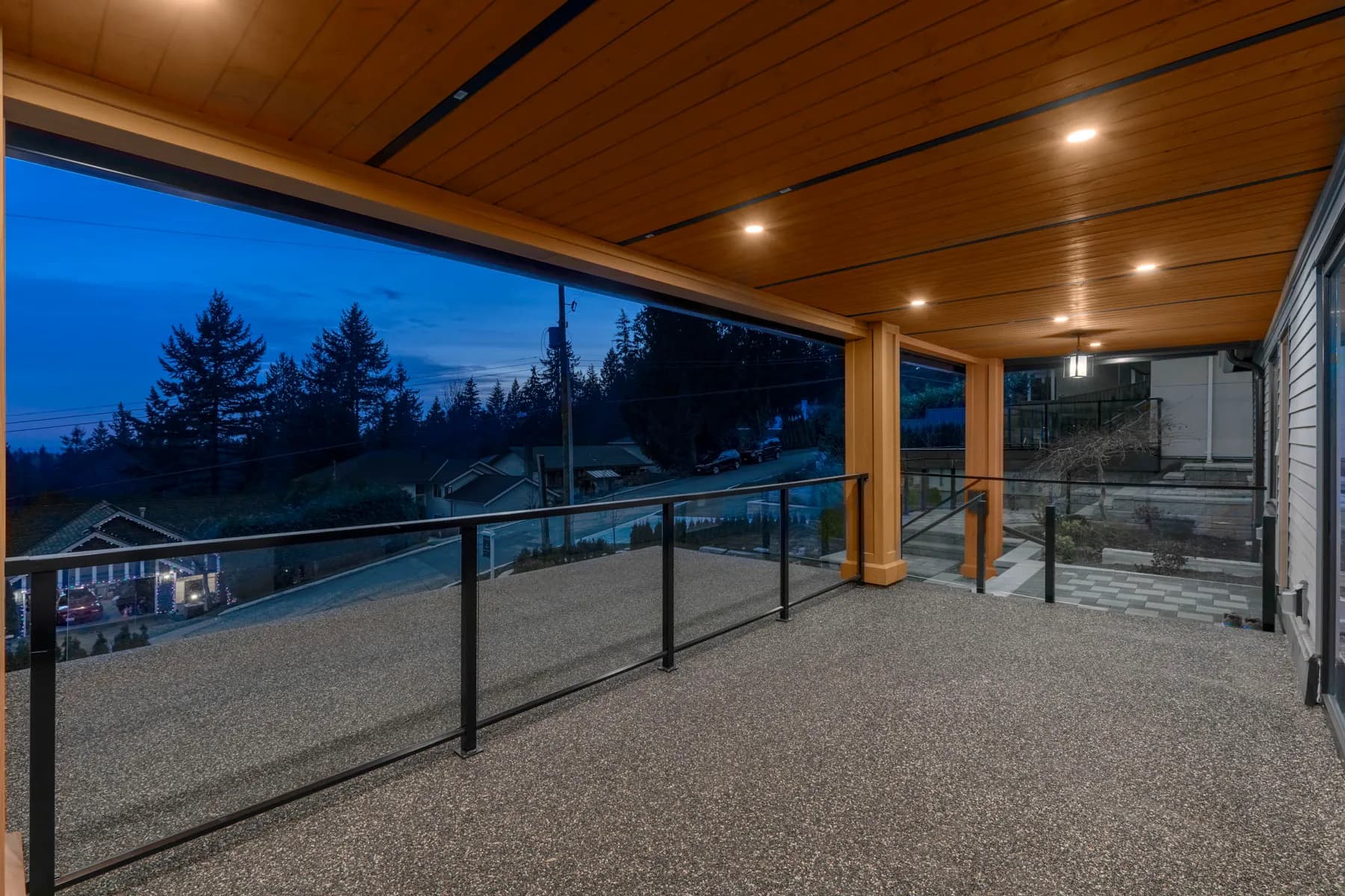 Covered deck at dusk with wood soffit, glass railings, and valley views