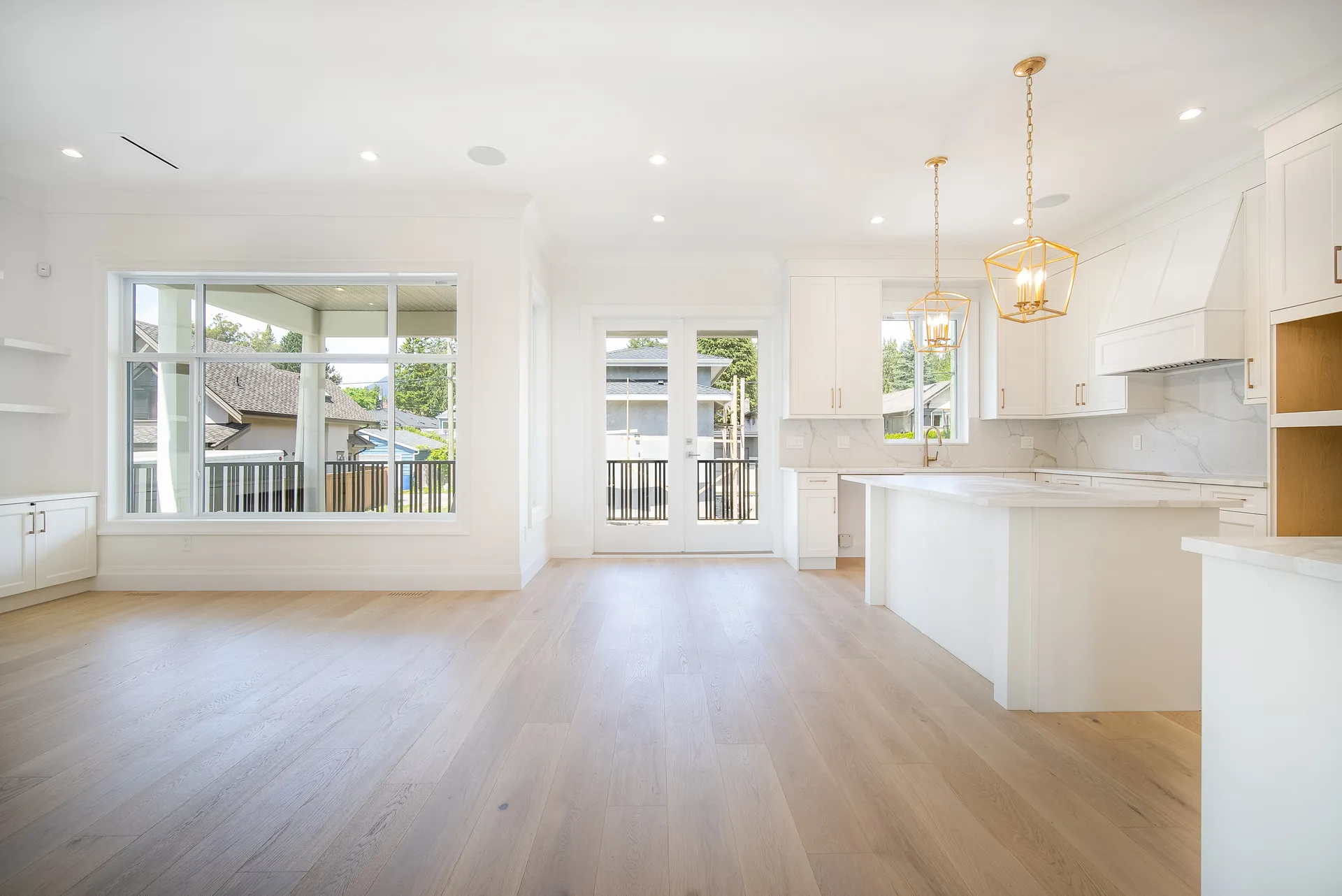 Open plan kitchen and living area with white cabinetry and gold pendants over the island in the Central Lonsdale Residence