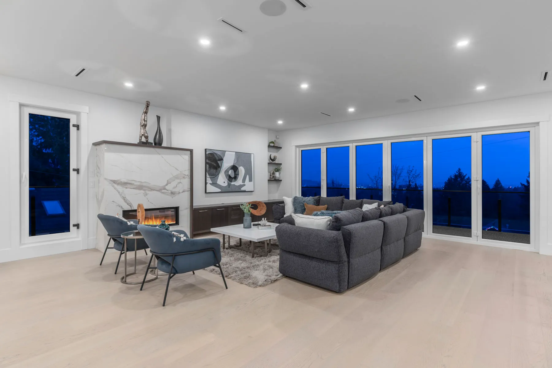 Living room with marble linear fireplace and full width windows at twilight in a Major Homes build